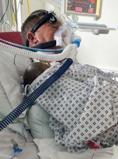 Man in hospital bed on a ventilator.