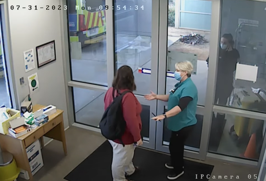 Two people wearing masks greet each other at a doorway.