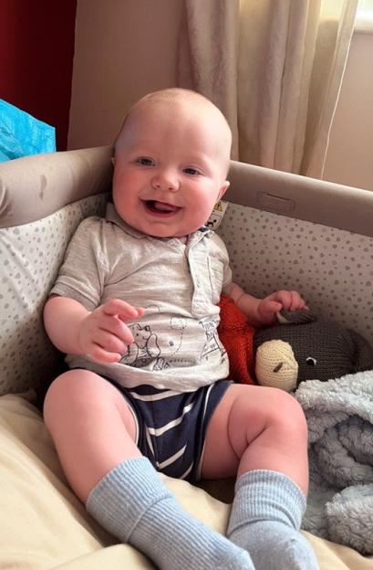 Six-month-old baby sitting in a crib, smiling.