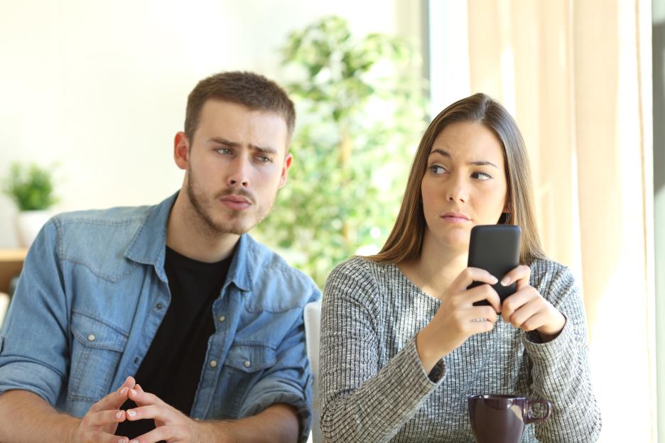 A jealous boyfriend watches his girlfriend looking at her phone.