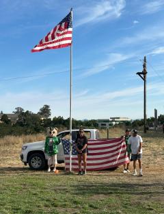 People standing with an American flag in front of a truck.