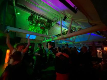 Crowded nightclub scene with green and purple lighting.