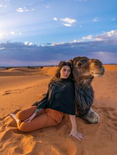 Woman sitting next to a camel in the desert.