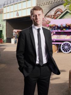 Portrait of Jamie Borthwick as Jay Brown in a black suit.
