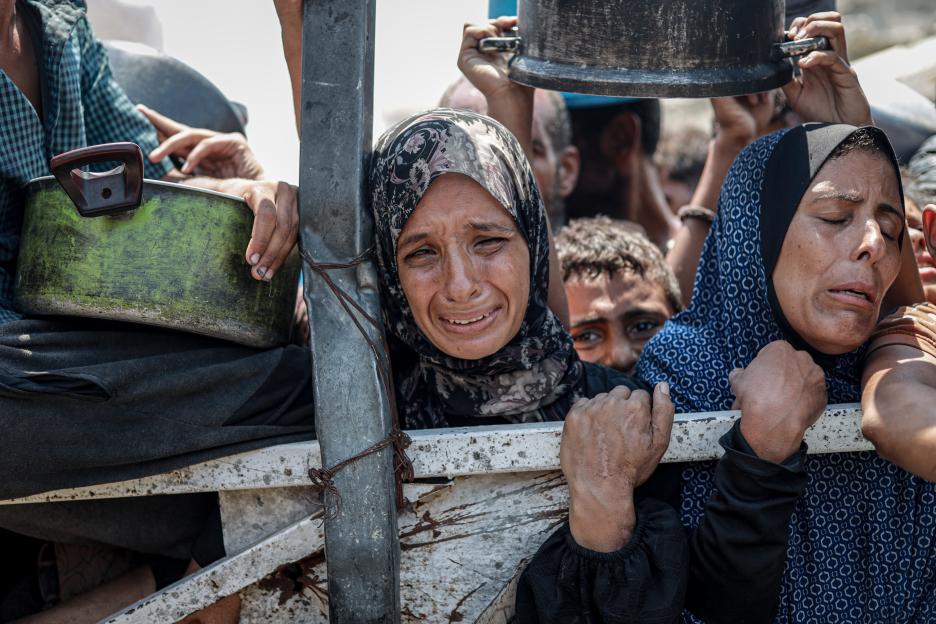 Palestinian women crying while waiting in line for food aid in Gaza.