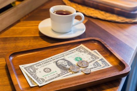 US dollar bills and coins on a wooden tray.