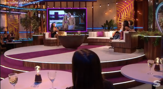 Screenshot of Love Island Aftersun set with guests on sofas and a large screen showing contestants.