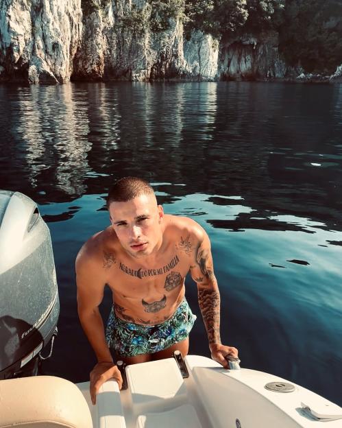 Man with tattoos emerging from the water onto a boat.
