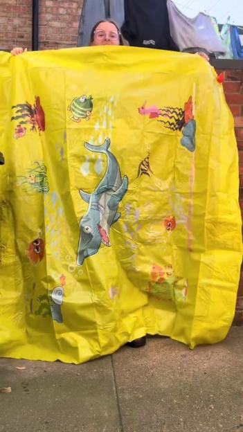 Person holding up a large yellow splash pad with underwater-themed illustrations.