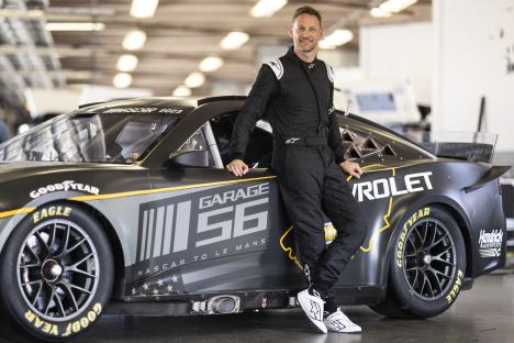 Jenson Button posing next to a NASCAR Garage 56 race car.