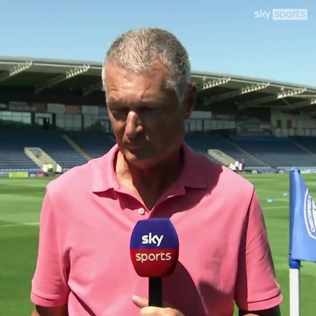 Sky Sports reporter holding a microphone at a soccer field.