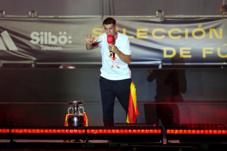 Man speaking into microphone on stage with trophy.