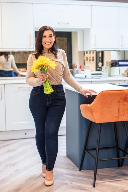 Woman holding daffodils in her kitchen.