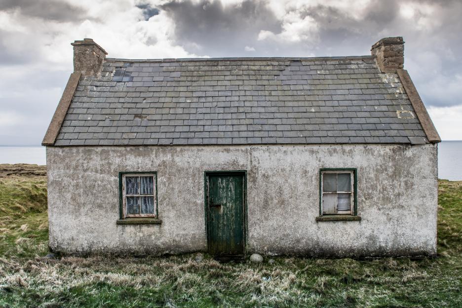 Old stone cottage on a grassy hillside overlooking the ocean.