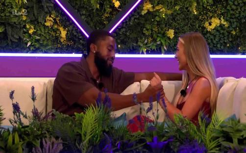 Remell and Poppy holding hands on a Love Island couch.