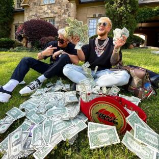 two men are sitting on the grass with a pile of money including one dollar bills