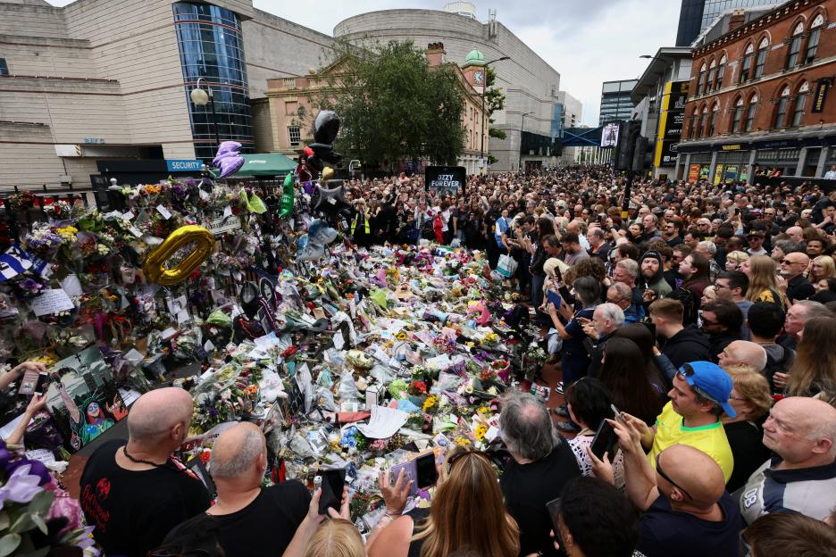 A crowd gathers around tributes at the Black Sabbath Bridge following Ozzy Osbourne's funeral.