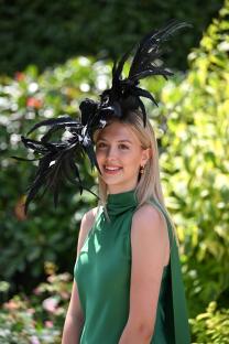 Holly Gilmer at Royal Ascot wearing a green dress and a large black feathered hat.