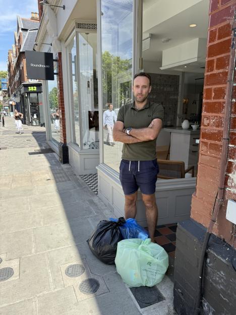 Man standing outside a shop with bin bags.