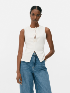Woman wearing a white sleeveless top and blue jeans.