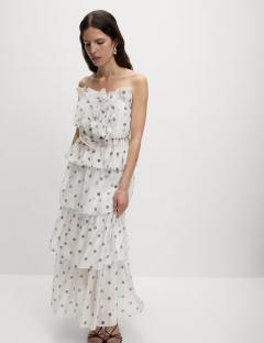 Woman wearing a white polka dot tiered maxi dress with a rose detail at the bodice.