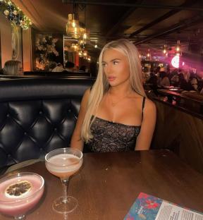 Woman sitting at a bar with two cocktails in front of her.