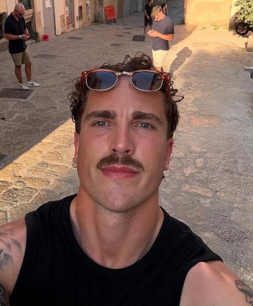 Selfie of a man with a mustache, wearing sunglasses, in a sun-drenched alleyway.