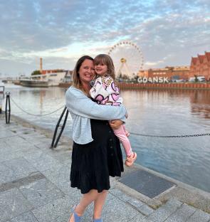 Woman holding a toddler in Gdansk, Poland, with a Ferris wheel in the background.