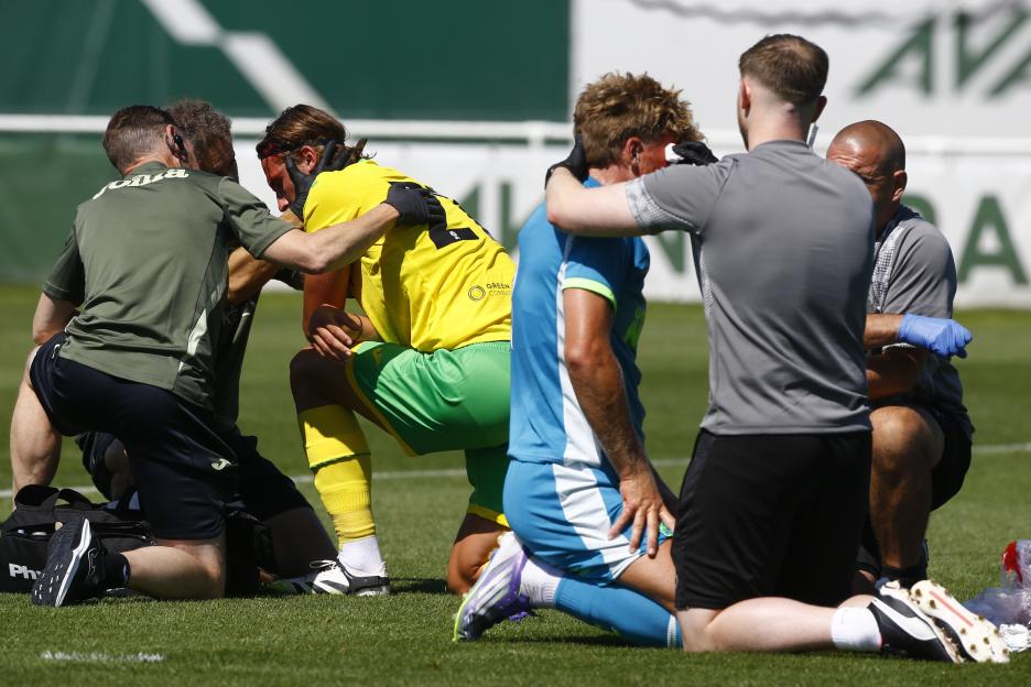 Two soccer players receiving medical attention on the field for head injuries.
