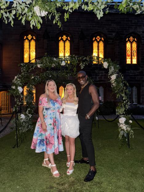 Three people posing in front of a flower arch at night.