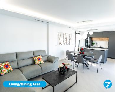Open-plan living and dining area with gray sofa, dining table, and modern kitchen.