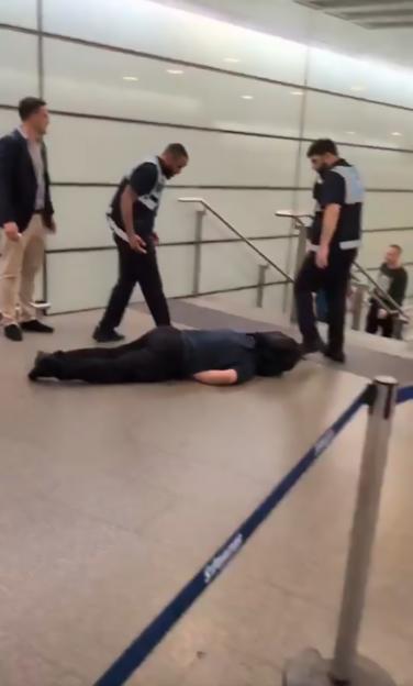 Person lying on the ground at St. Pancras railway station with security personnel nearby.