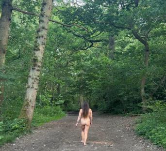 A naked woman walks down a wooded path.