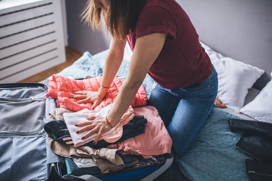 One young woman in her bedroom, packing suitcase for vacation.