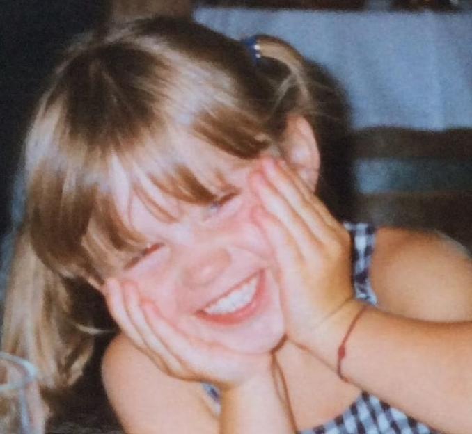 Young girl smiling with hands on cheeks.
