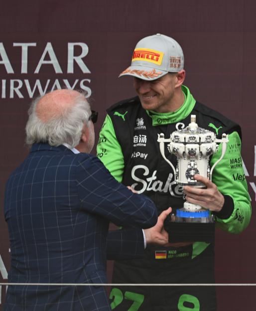 Nico Hulkenberg receiving a trophy on a Formula 1 podium.
