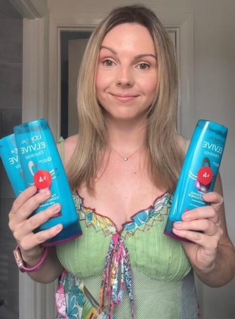 Woman holding two bottles of L'OrÃ©al Elvive hair conditioner.