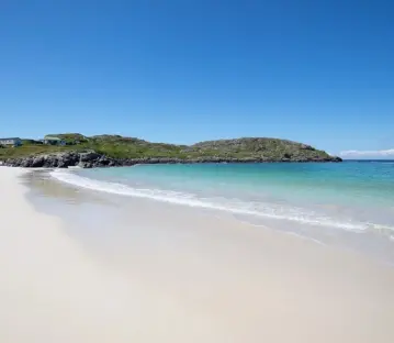 White sand beach and turquoise water with a small hill in the background.