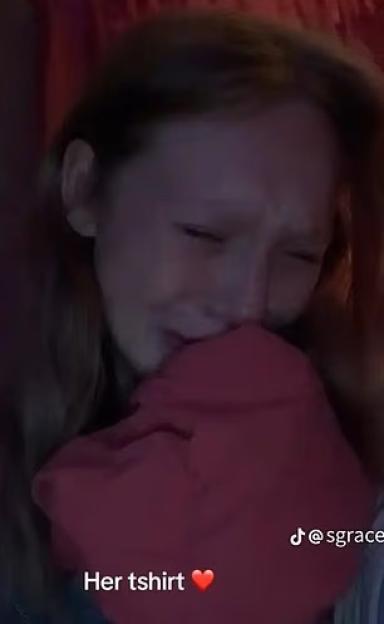 Teenage girl crying, covering her face with a pink shirt.