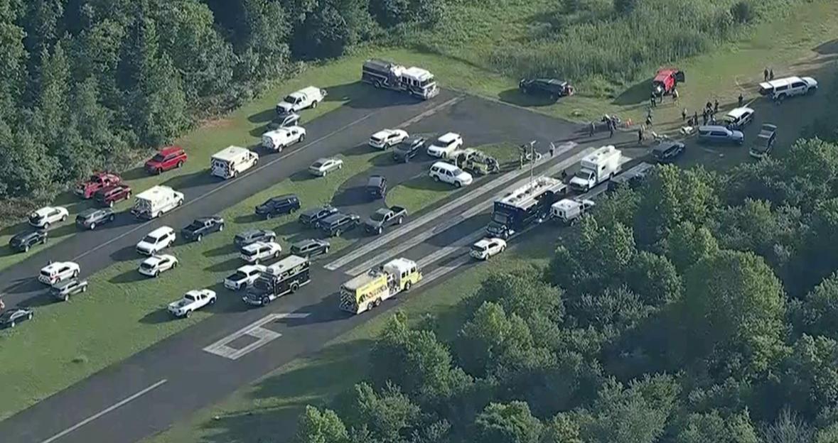 Aerial view of emergency personnel and vehicles at an airport runway after a small aircraft crash.