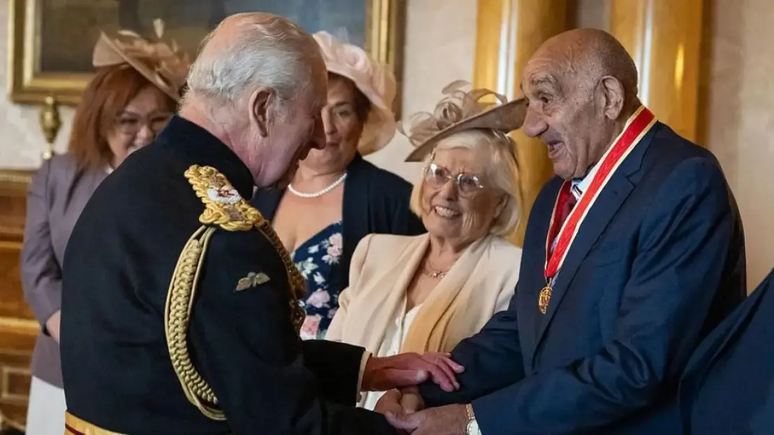King Charles III bestowing an honor on Sir Billy Boston.