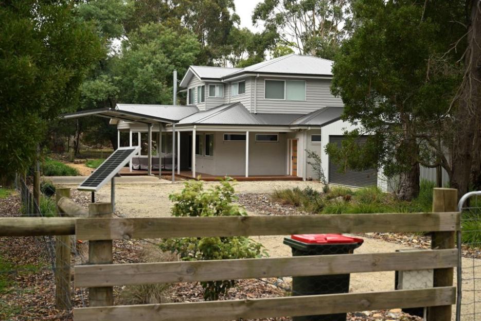 Modern house with solar panel and carport, viewed through a wooden fence.