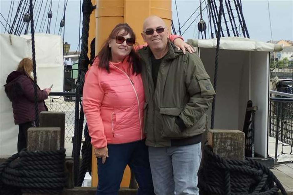 A man and woman stand arm in arm on a ship's deck.