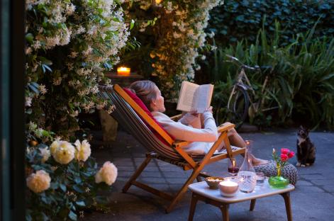 Woman relaxing in a deck chair, reading a book in a garden at night.