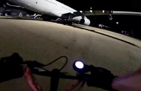 First-person view of a person riding a scooter at night near a large airplane.