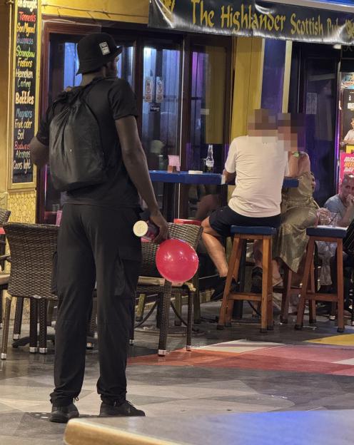 A person selling nitrous oxide balloons outside a bar.