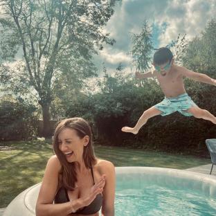 Woman laughing in a hot tub as a boy jumps over her.