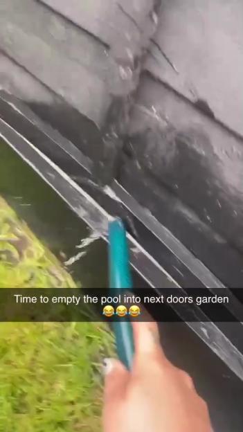 A hand using a hose to drain a pool into a neighbor's yard.