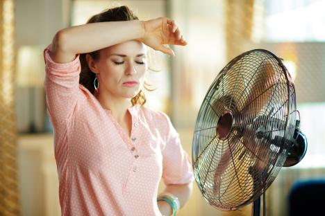 Woman standing in front of a fan, wiping sweat from her forehead.