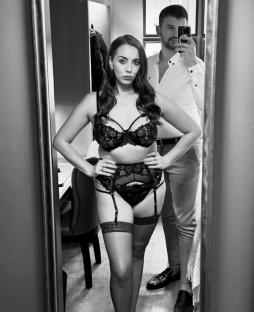 Black and white photo of a couple reflected in a mirror; the woman is wearing lingerie.